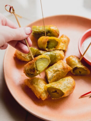 A plate of fried paper fried pickles sliced in half with one being held up by a tooth pick.