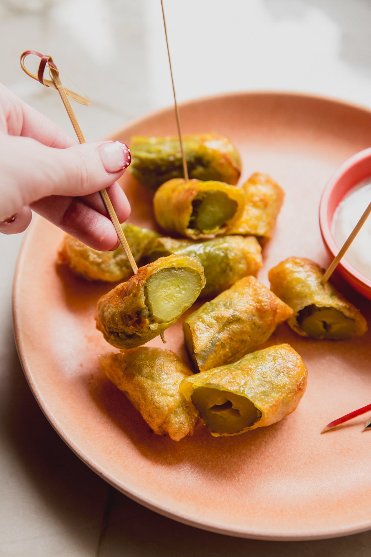 A plate of fried paper fried pickles sliced in half with one being held up by a tooth pick.