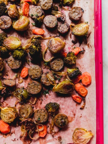 one pan sausage and vegetables cooked on a pink baking sheet.