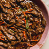 Slow cooker mongolian beef with carrots and green onions in a pink bowl.