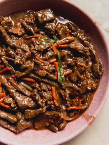 Slow cooker mongolian beef with carrots and green onions in a pink bowl.