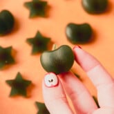 Green apple shaped gummy being held.