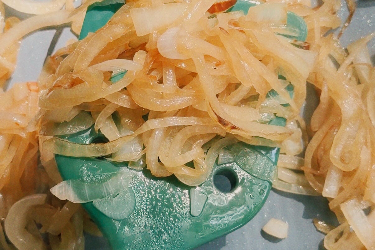 A pan with sauted onions and a green spatula stirring it.