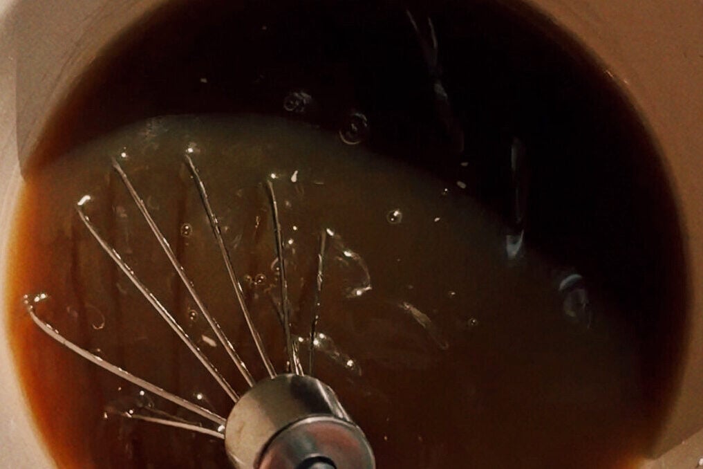 A whisk mixing the suace in a white bowl.