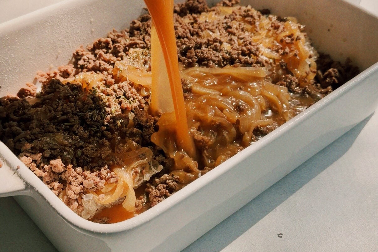 Sauce being poured over a casserole dish filled with ground beef, onions, and ramen.