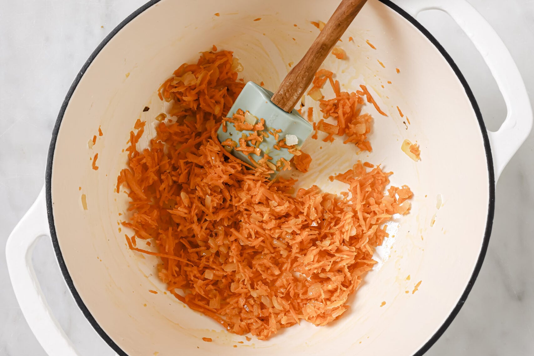 Shredded carrots being cooked in a white pot.