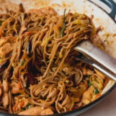 Chicken yakisoba in a large cast iron pan with tongs pulling up the noodles