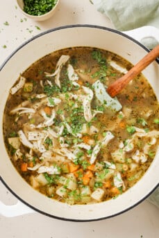 Chickpea chicken soup topped with chopped parsley in a white dutch oven.