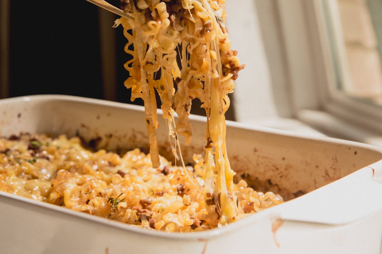 A serving utensil pulling out a serving of French onion ramen bake from the finished casserole.