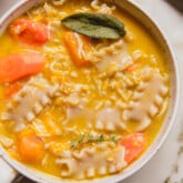 Pumpkin chicken noodle soup topped with sage in a white bowl