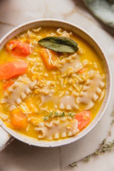 Pumpkin chicken noodle soup topped with sage in a white bowl