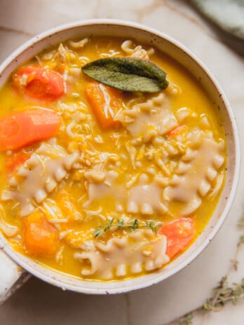 Pumpkin chicken noodle soup topped with sage in a white bowl