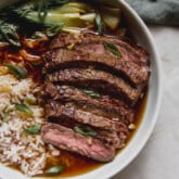 Sliced steak, rice, and veggies in a bowl with broth.