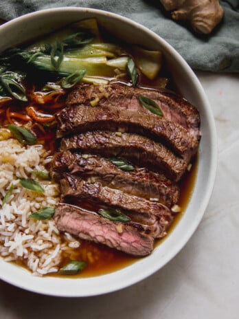 Sliced steak, rice, and veggies in a bowl with broth.