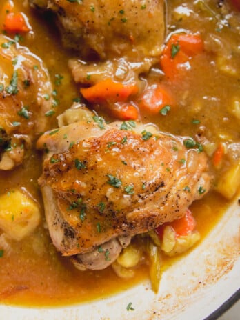 Pot roast chicken thighs with vegetables and gravy in a cast iron pot