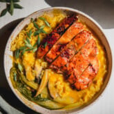 Pumpkin ramen in a bowl with bok choy, ramen noodles, an orange broth, and sliced chicken on top.