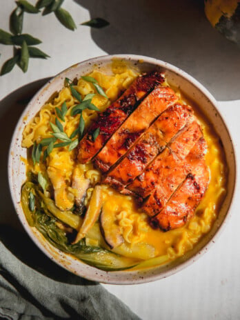 Pumpkin ramen in a bowl with bok choy, ramen noodles, an orange broth, and sliced chicken on top.